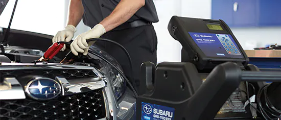 A Subaru service technician checking a battery with a machine.